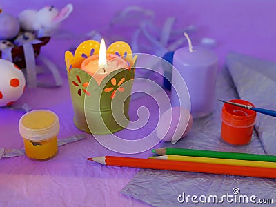 Easter decor, painted eggs, paints, brushes, lighted pink candles on a lilac background, preparation for the Easter holiday Stock Photo