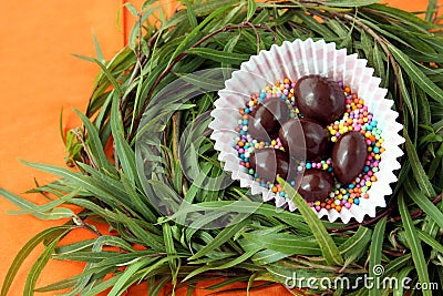 Easter decoration: chocolate eggs in green grass twigs nest on orange background Stock Photo