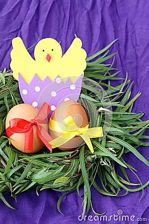 Easter decoration: yellow eggs and hand made hatched chicken in eggshell in green grass twigs nest on purple background Stock Photo