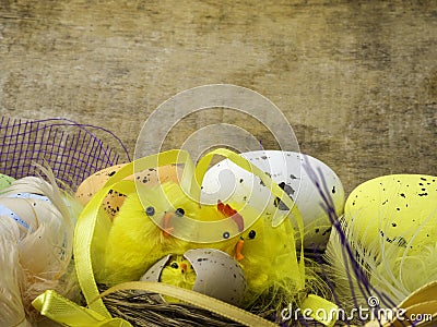 Easter decorative composition with yellow chickens nest, color eggs and colorful feathers on wooden board Stock Photo