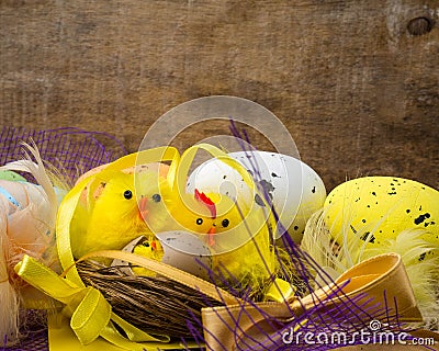 Easter decorative composition with yellow chickens nest, color eggs and colorful feathers on wooden board Stock Photo