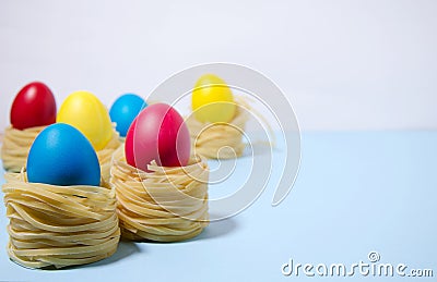 Easter eggs of blue, red, yellow color stand in pasta nests on a blue white background horizontal background Stock Photo