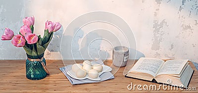 Easter eggs, book and pink tulips on table. Simple holiday image Stock Photo