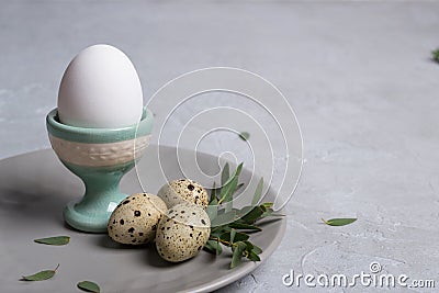 Easter festive table setting with gray plate, quail eggs and chicken egg standing in the egg cup with leaf sprigs of eucalyptus Stock Photo