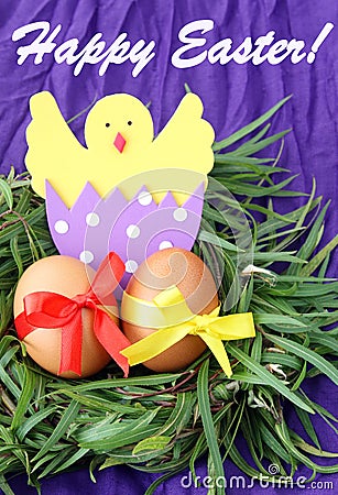 Easter hand made decorated greeting card: yellow eggs and hand made hatched chicken in eggshell in green grass twigs nest on purpl Stock Photo