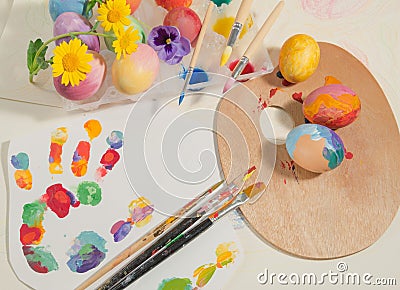 Easter hand-painted eggs with painter brushes,wooden palette,watercolors and spring flowers,arranged on colored fingerprints. Stock Photo