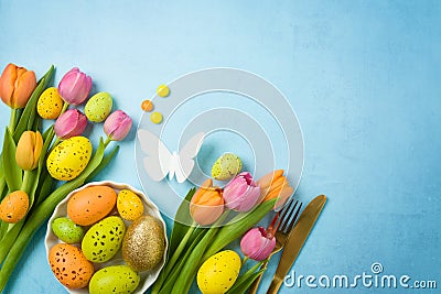 Easter holiday celebration concept with easter eggs gold flatware and tulip flowers on blue background. Top view, flat lay Stock Photo