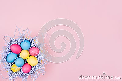 Easter painted eggs in fun blue nest on soft pink background, copy space, top view. Stock Photo