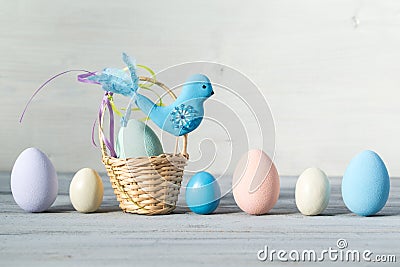 Easter pastel colored eggs and small basket with blue bird on a light wooden background Stock Photo