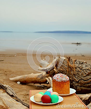 Easter picnic: Easter cake and colored eggs on white plates on a blurred background of the sandy banks of the Volga River Stock Photo