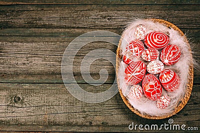 Easter red eggs with folk white pattern lay on feather into basket in the right side of rustic wood table. Top view. Ukrainian tra Stock Photo