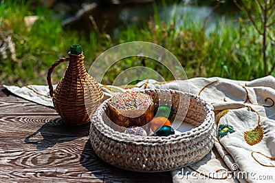 Easter still life as jug and knitted pottle with colored eggs inside stays on the aged wooden table with tablecloth under blooming Stock Photo