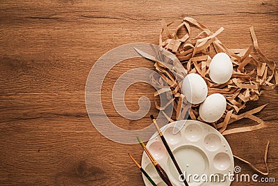 Easter, eggs on brown paper, paintbrush and color dish on wooden table Stock Photo