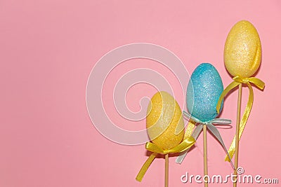 Eastern eggs with ribbon on stick, yellow, blue on pink background Stock Photo
