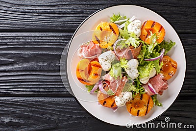 Easy dietary salad with mozzarella, prosciutto, grilled apricots, red onion and lettuce close-up on a plate. horizontal top view Stock Photo