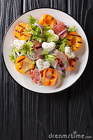 Easy dietary salad with mozzarella, prosciutto, grilled apricots, red onion and lettuce close-up on a plate. Vertical top view Stock Photo