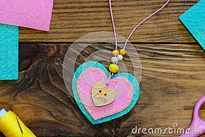 Easy felt heart pendant necklace. Valentines day felt pendant necklace with beads and wooden button. Kids creative workplace Stock Photo