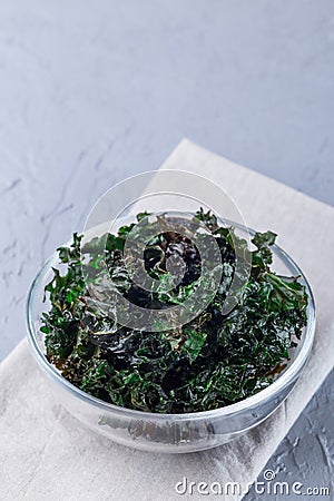 Easy three ingredient baked green kale chips with sea salt and olive oil, in glass bowl, vertical, copy space Stock Photo