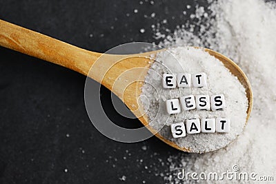 Eat less salt in order to reduce blood pressure or hypertension risk with sprinkled salt on dark background Stock Photo