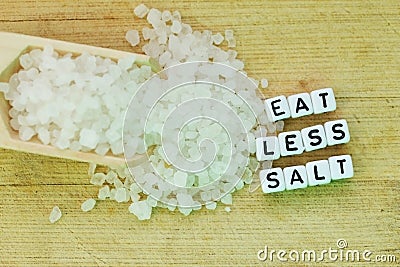 Eat less salt recommendation with plastic letters and granulated salt on wooden chopping board Stock Photo