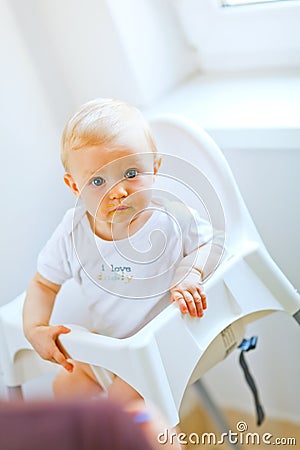 Eat smeared baby in chair interestedly looking Stock Photo