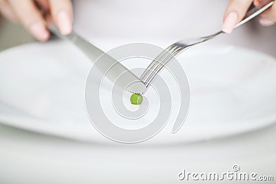 Eating disorder. Girl is holding a plate and trying to put a pea Stock Photo