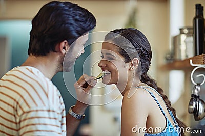 Eating healthy together. an affectionate young couple snacking while preparing a meal in their kitchen. Stock Photo