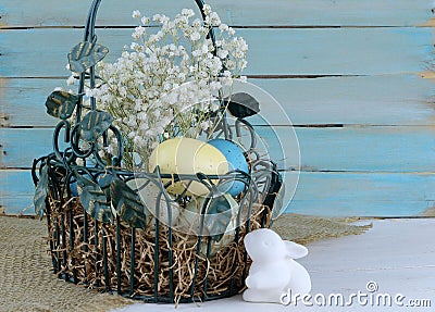 Eatser image includes a green, wire basket with colorful spotted eggs and baby`s breath on a rustic wooden background. Stock Photo