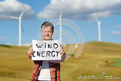 Eco activist with banner `Wind Energy` on background of power stations for renewable electric energy production. Stock Photo