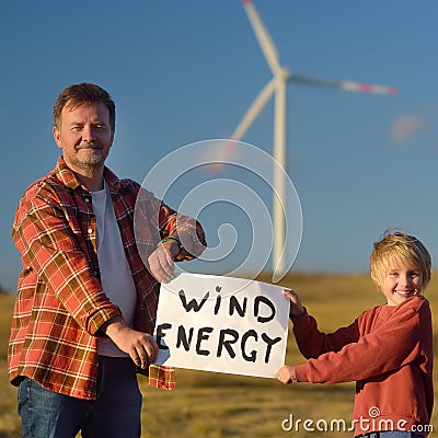 Eco activists with banner `Wind Energy` on background of power stations for renewable electric energy production. Stock Photo