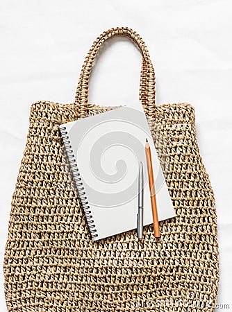 Eco bag made of straw and a clean notepad on a white background, top view. Shopping planning concept Stock Photo