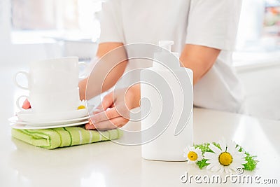 Eco friendly cleaning dish soap with natural chamomile flower ingredient and woman putting clean white cups and plates Stock Photo
