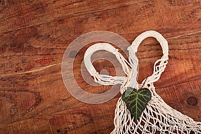 Eco friendly string bag and green leaf on wooden background, responsible consumption. zero waste concept. Stock Photo