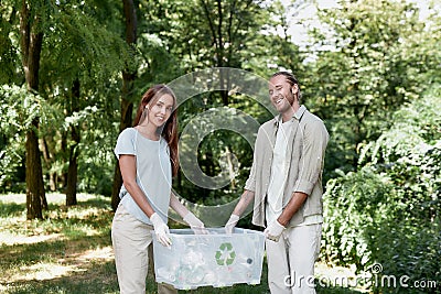 Eco volunteering. Young cheerful couple holding recycle bin and smiling at camera while cleaning together green forest Stock Photo