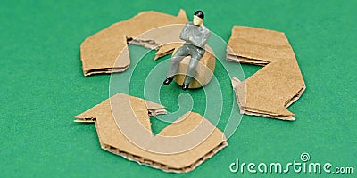On the green surface lies the symbol of recycling, in the middle of the cube sits a miniature human figurine. Stock Photo