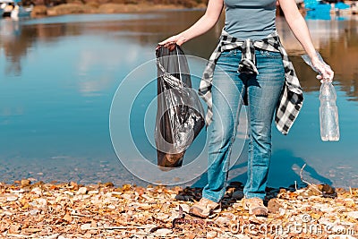 Ecology and garbage collection. Woman volunteer with a garbage bag in his hands, engaged in garbage collection on the lake or sea Stock Photo