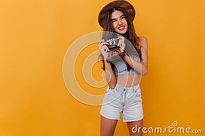 Ecstatic brunette female photographer posing with cute smile. Indoor portrait of elegant slim girl with camera standing Stock Photo