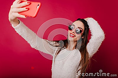 Ecstatic brunette girl plays with her hair while taking picture of herself. Indoor photo of inspired woman in heart Stock Photo