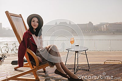 Ecstatic brunette girl posing with pleasure in chaise-longue. Outdoor portrait of smiling lady in recliner sitting on Stock Photo