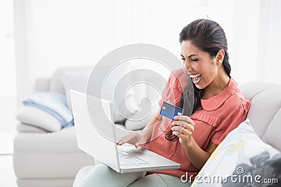 Ecstatic brunette sitting on her sofa using laptop to shop online Stock Photo
