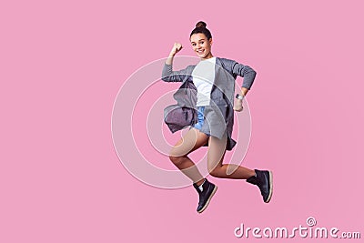 Ecstatic brunette teenage girl jumping in the air with enthusiastic happy face. indoor studio shot isolated on pink background Stock Photo