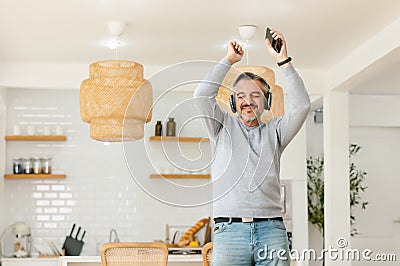 Ecstatic excited grey-haired man in casual and wireless headphones enjoy spare time, listen favorite music and dancing in front Stock Photo