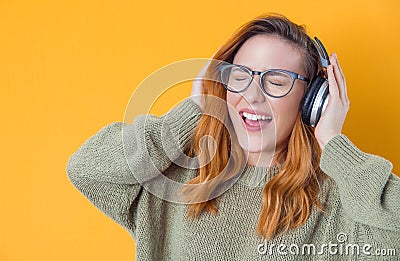 Ecstatic girl with headphones enjoying while listen music isolated on yellow background. Joyful woman with earphones. Happiness Stock Photo