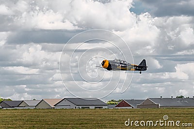 AT-6 Texan Flies Low Over Runway with Hangers Editorial Stock Photo