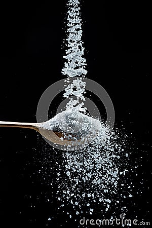 Edible salt crystals falling down into the wooden spoon at black background Stock Photo