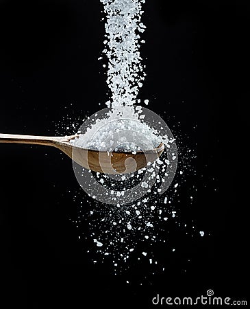 Edible salt crystals falling down into the wooden spoon at black background Stock Photo