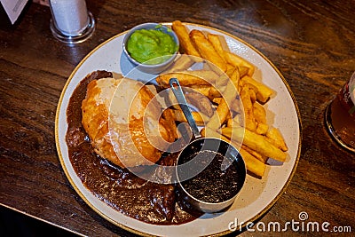 Traditional steak and ale pie and a pint in a Scottish pub with chips, gravy and mushy peas Stock Photo