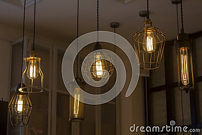 Edison`s antique lamps of various shapes and sizes in lampshades glow in the dark under the ceiling Stock Photo