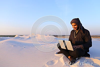 Educated Arab student uses laptop and works sitting on sand amid Stock Photo
