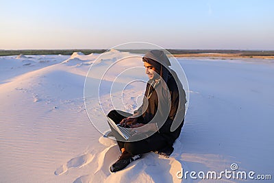 Educated Arab student uses laptop and works sitting on sand amid Stock Photo